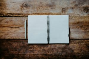 Caderno espiral aberto com páginas pautadas em branco ao lado de uma caneta sobre mesa de madeira rústica, representando o início de uma escrita profissional.