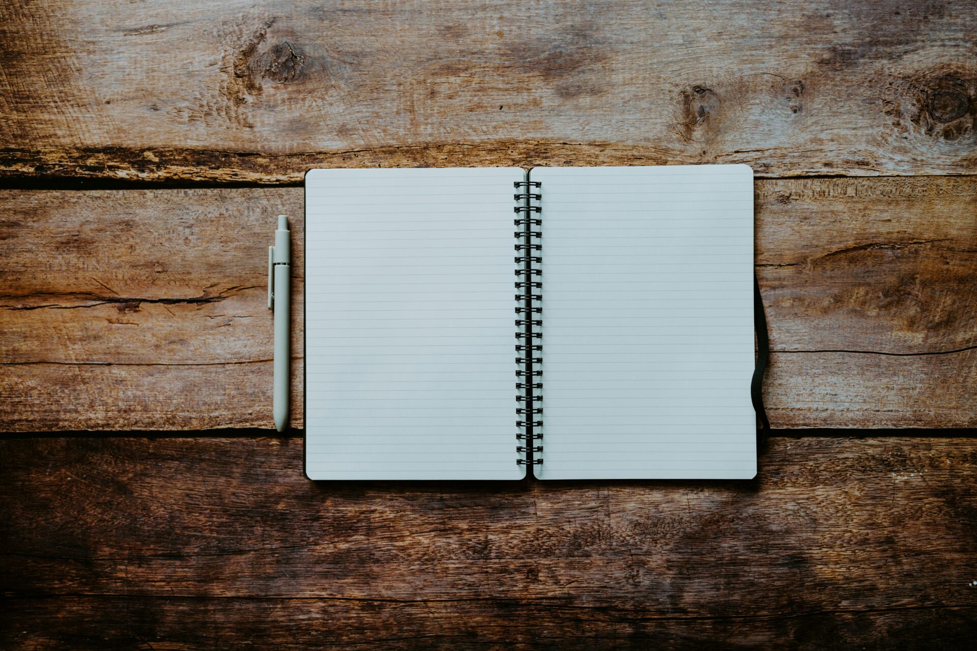 Caderno espiral aberto com páginas pautadas em branco ao lado de uma caneta sobre mesa de madeira rústica, representando o início de uma escrita profissional.