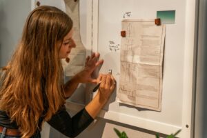 Mulher jovem escrevendo planejamento estratégico em quadro branco com anotações de comunicação digital.